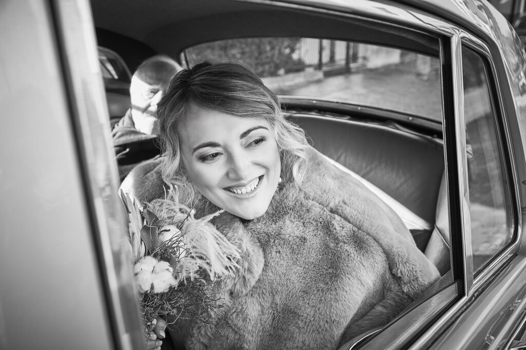 Bride smiling inside the wedding car with her bouquet