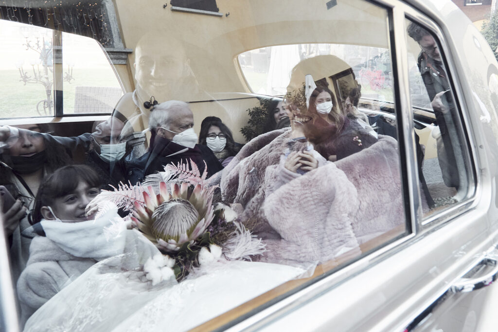 Bride inside the wedding car surrounded by reflections of family and guests