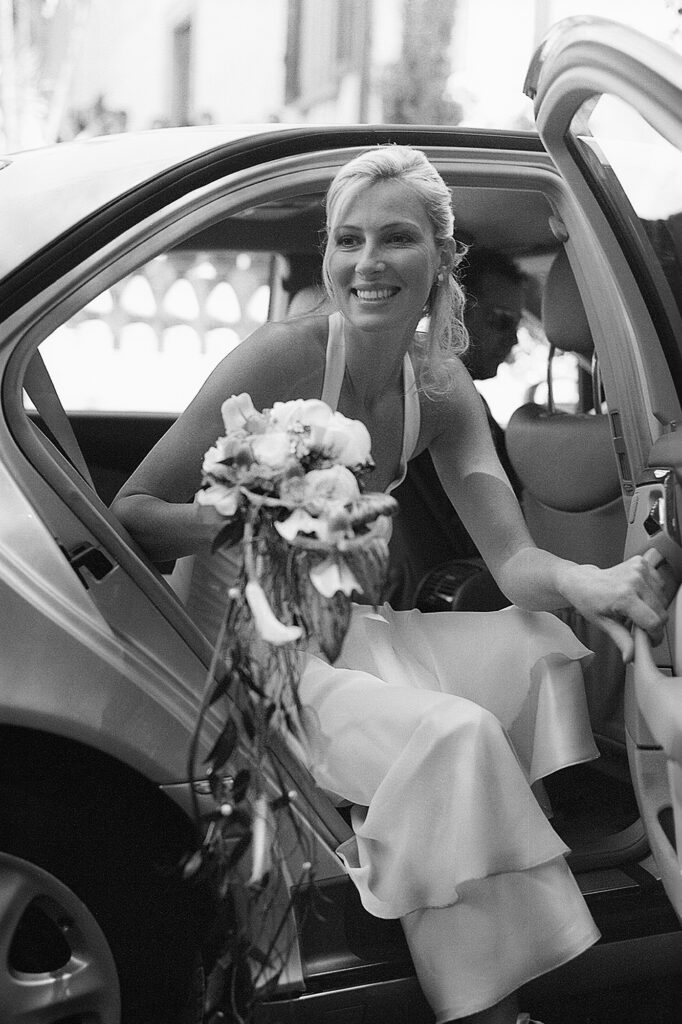 Bride smiling as she steps out of the car with her wedding bouquet